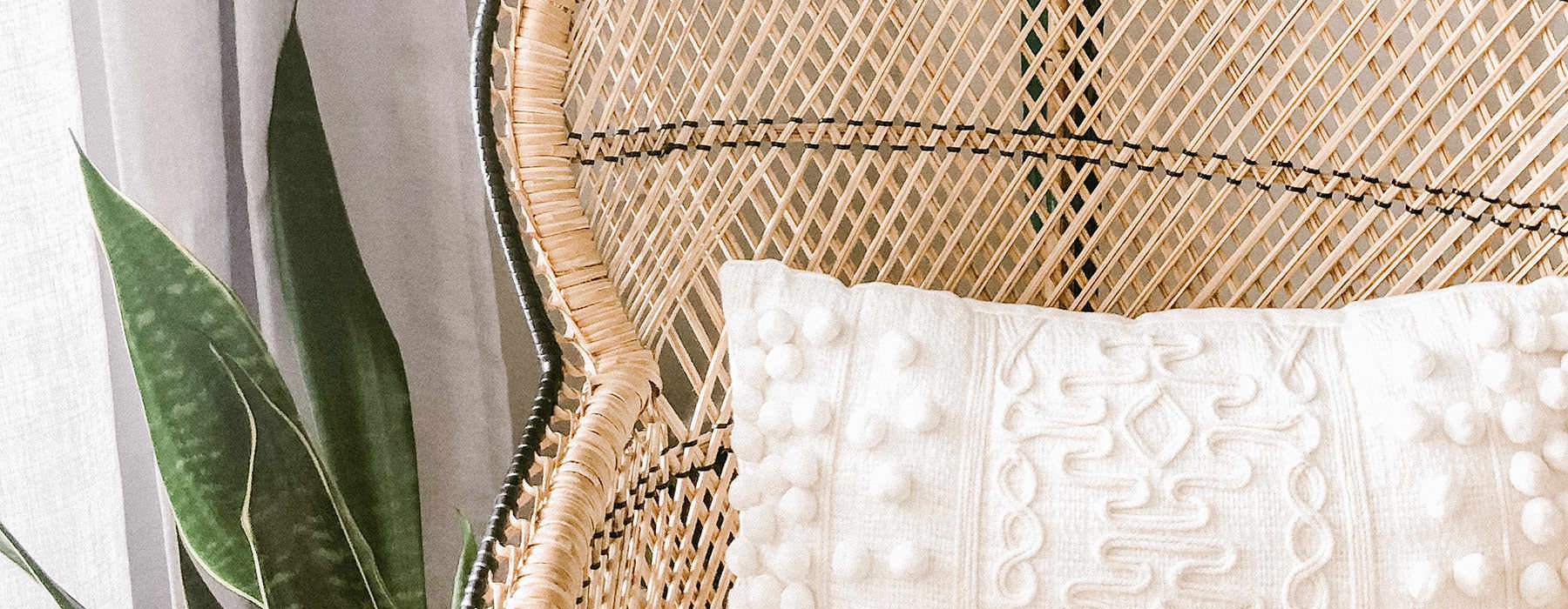 wicker chair with a pillow next to potted, indoor plant